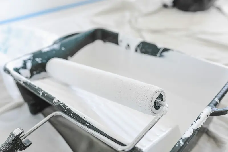 Rouleau de peinture blanche posé dans son bac